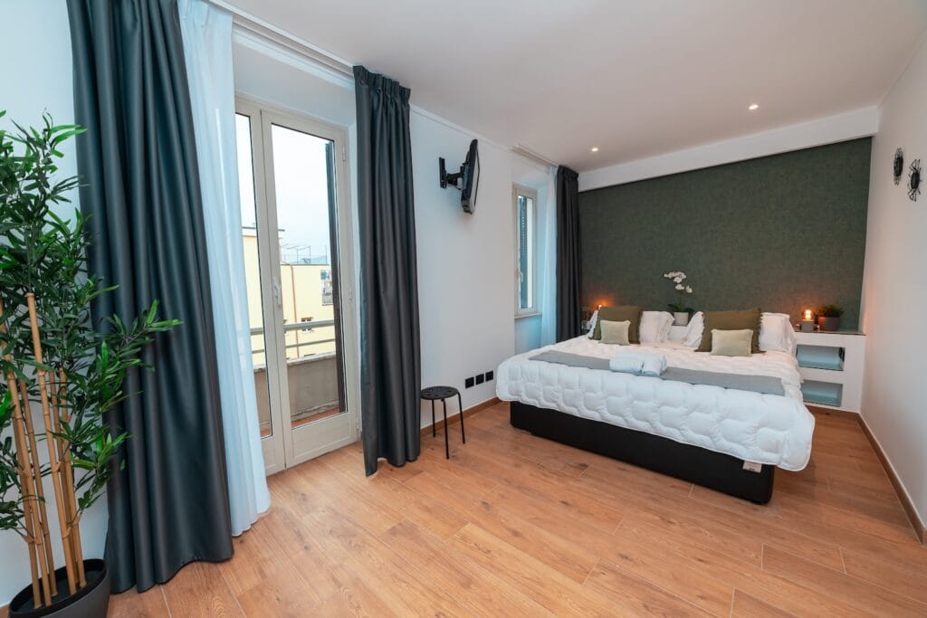 Dettaglio di una camera a Roma con panoramica sulla camera da letto e sulla scrivania, con finestre e tende aperte
