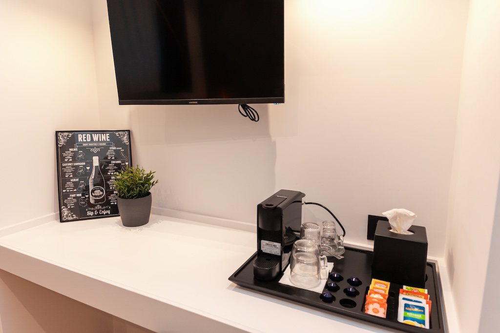 Dettaglio di una camera a Roma con scrivania e macchina del caffè, cialde, bicchieri e TV a muro