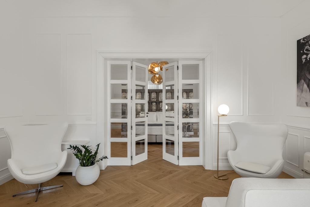Dettaglio della porta in vetro che separa il soggiorno dalla camera da letto dell'elegante suite Nora con poltrone e lampade moderne