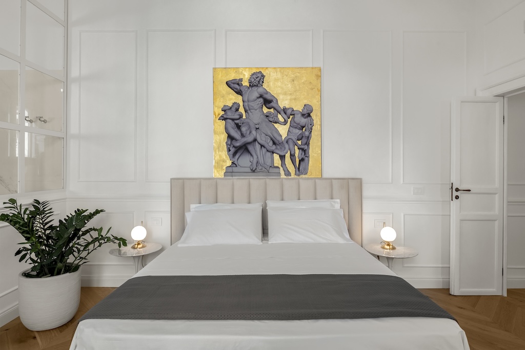 Dettaglio del letto dell'elegante suite Laura con letto, lampade moderne e capezzale artistico