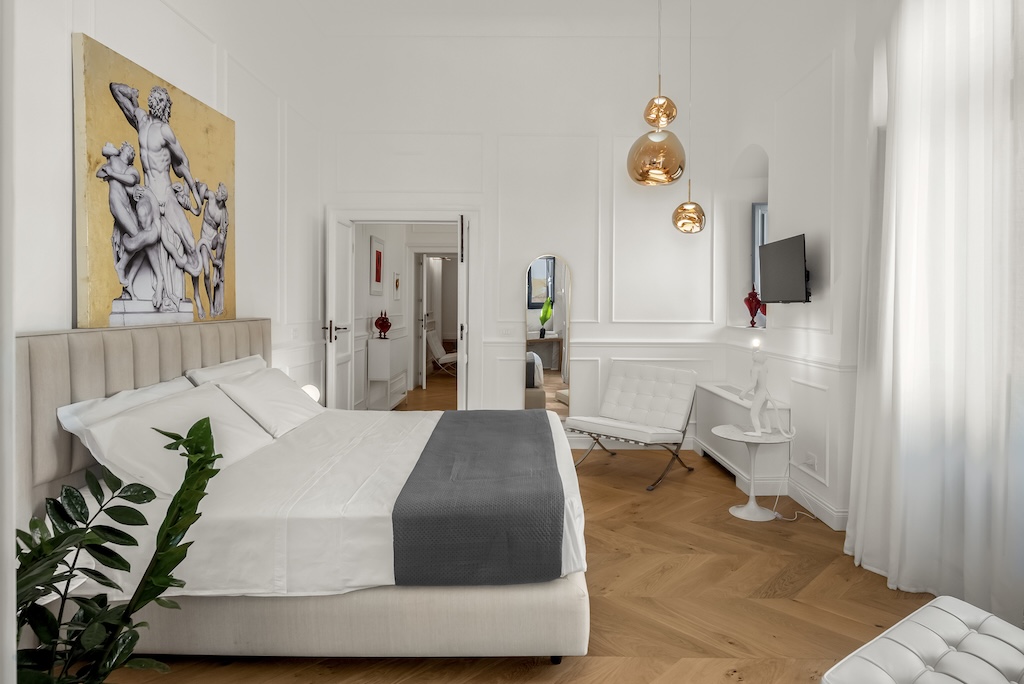 Panoramica della camera da letto dell'elegante suite Laura con letto, poltroncine, TV a muro e design artistico