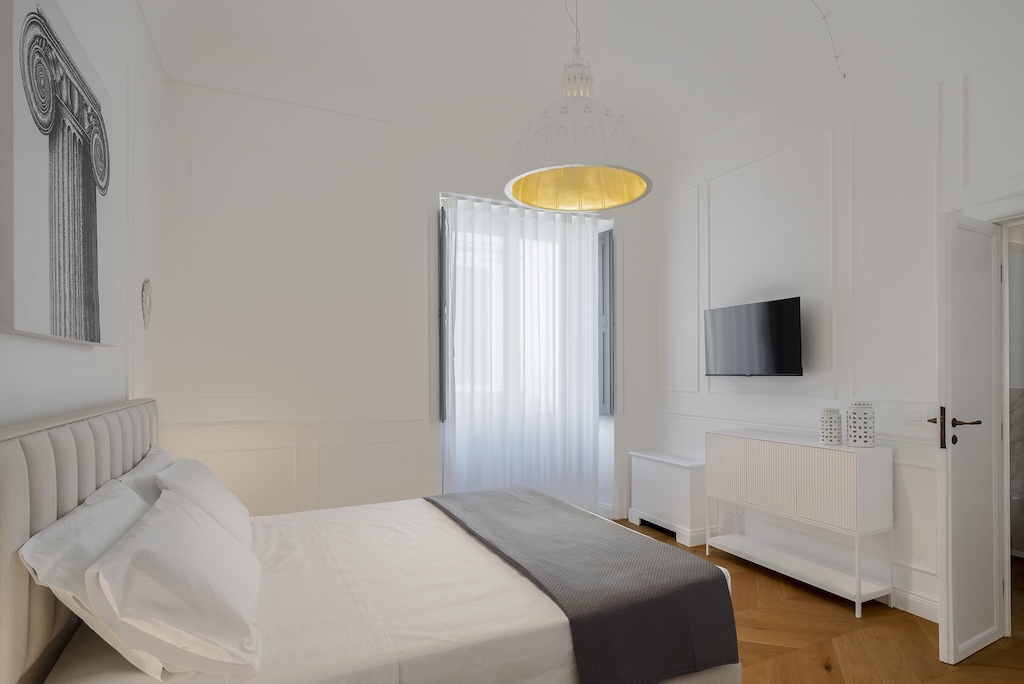 Dettaglio della camera da letto dell'elegante suite Christine con letto, lampada moderna e finestra con vista sulla città di Noto