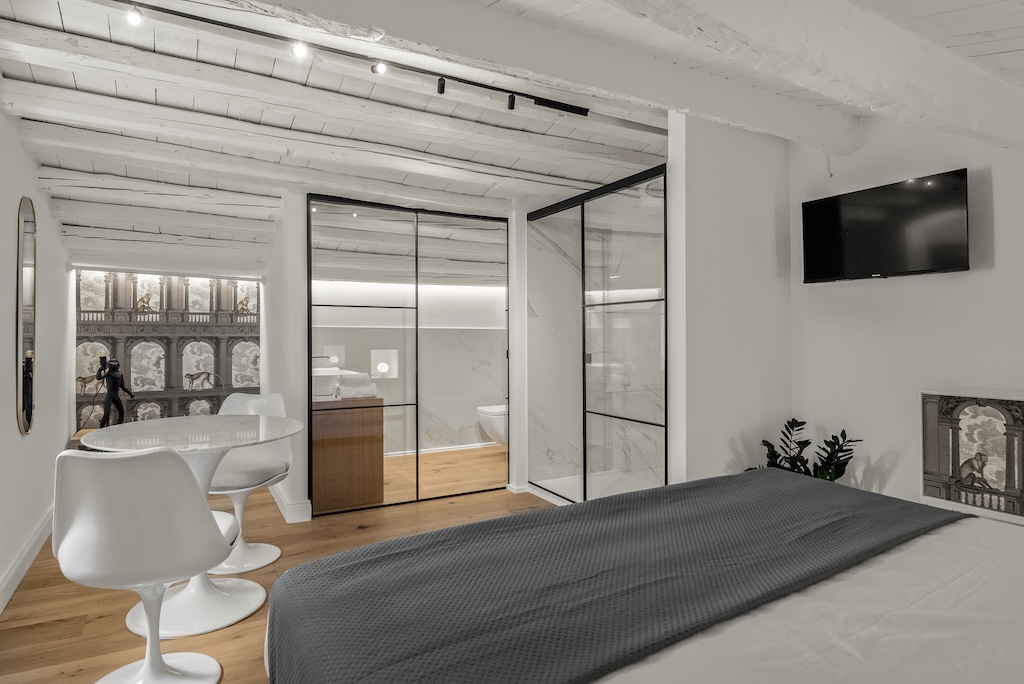 Panoramica della camera mansardata Carla con letto, zona giorno, TV a muro, doccia e bagno